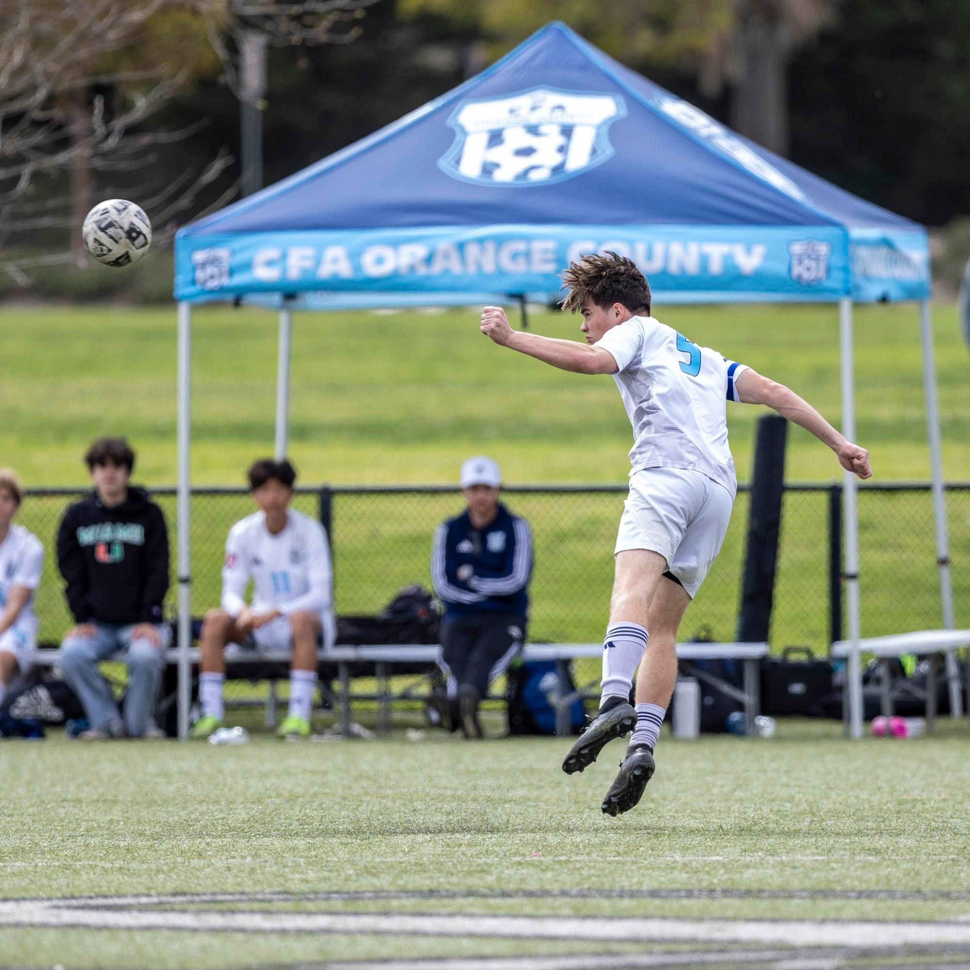 CFA boys player in white heading the ball in front of the club tent