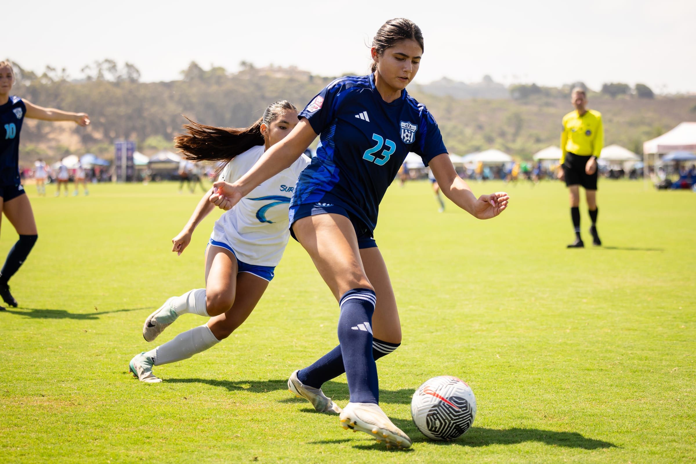 CFA girls player in navy driving forward with the ball past a defender