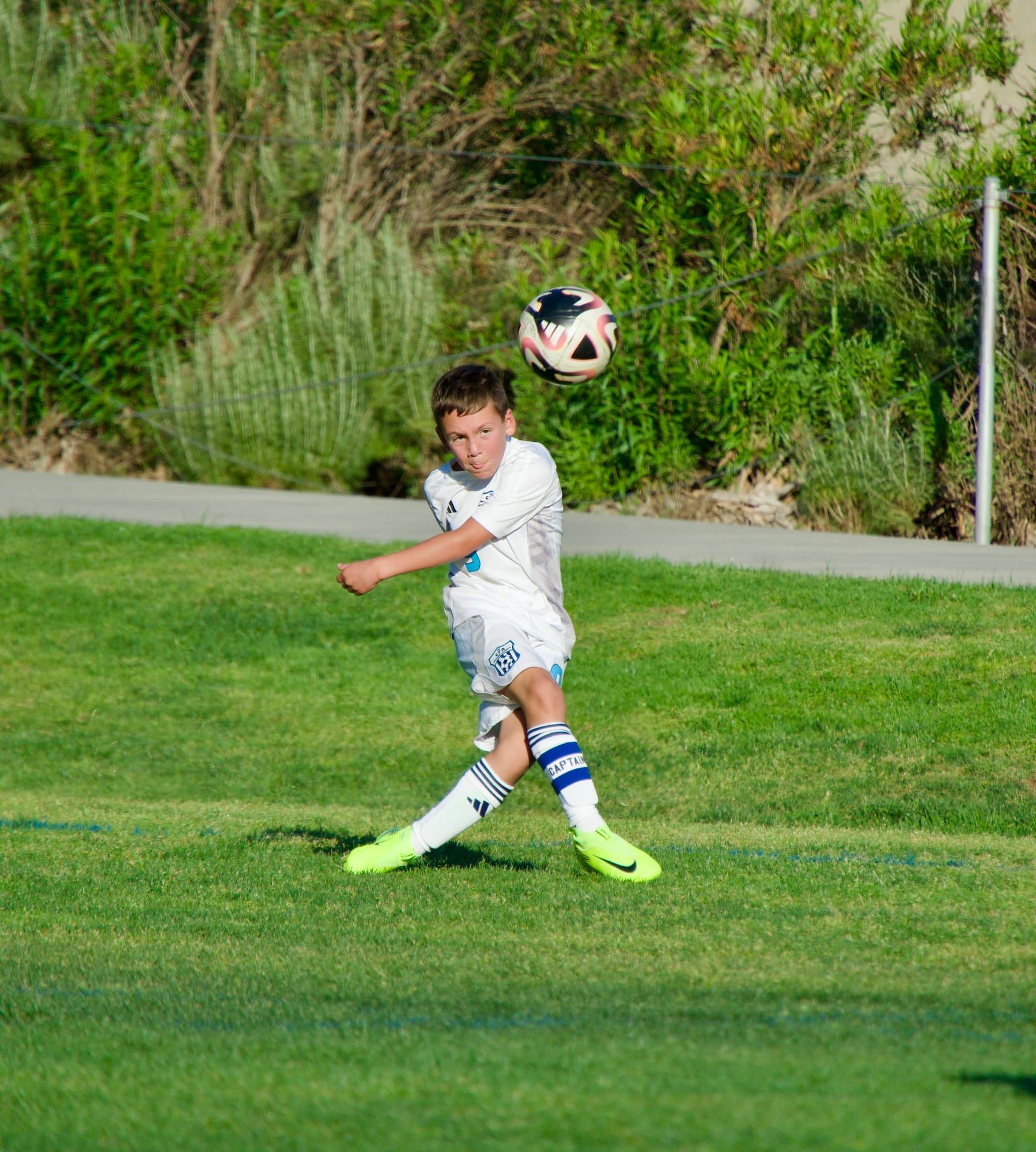 Young CFA boys player in white volleying a high ball